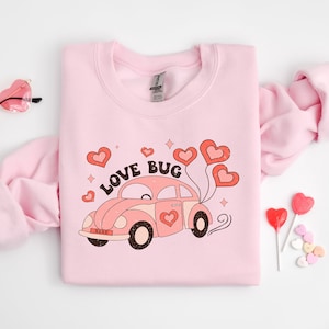 May include: Pink sweatshirt with a graphic of a pink car with the text "LOVE BUG" and red hearts.