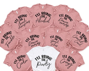 May include: Nine pink t-shirts with black text that reads "I'll bring the..." followed by a different phrase on each shirt. The phrases are "bad decisions", "trouble", "dance moves", "good vibes", "credit card", "calm", "crazy", "alcohol", and "dance moves". One white t-shirt with black text that reads "I'll bring the party".
