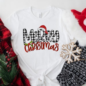 May include: White t-shirt with a black and white buffalo plaid "Merry Christmas" graphic with a red Santa hat on top of the "M".