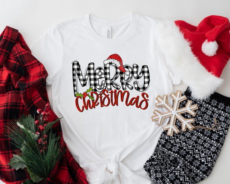 May include: White t-shirt with a black and white buffalo plaid "Merry Christmas" graphic with a red Santa hat on top of the "M".