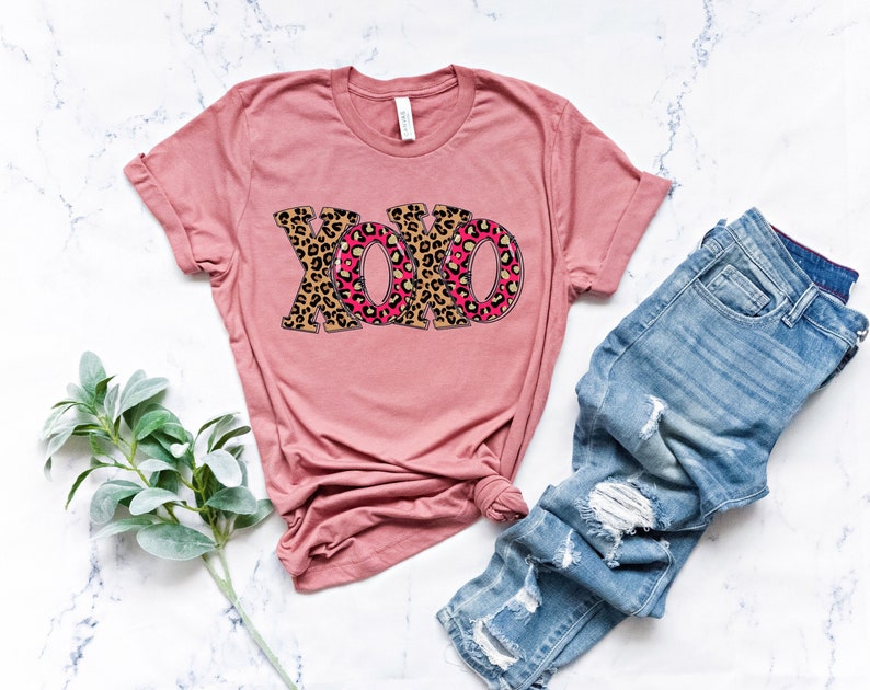 May include: A pink t-shirt with a leopard print "XOXO" graphic. The shirt is made of a soft, comfortable material and has a relaxed fit.