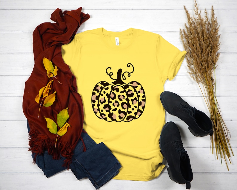 May include: A yellow t-shirt with a black and brown leopard print pumpkin graphic. The pumpkin has a stem and curly vines.
