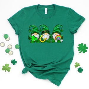 Peut inclure: T-shirt vert avec un motif de trois gnomes portant des chapeaux verts, tenant un fer &agrave; cheval, un arc-en-ciel et un tr&egrave;fle.