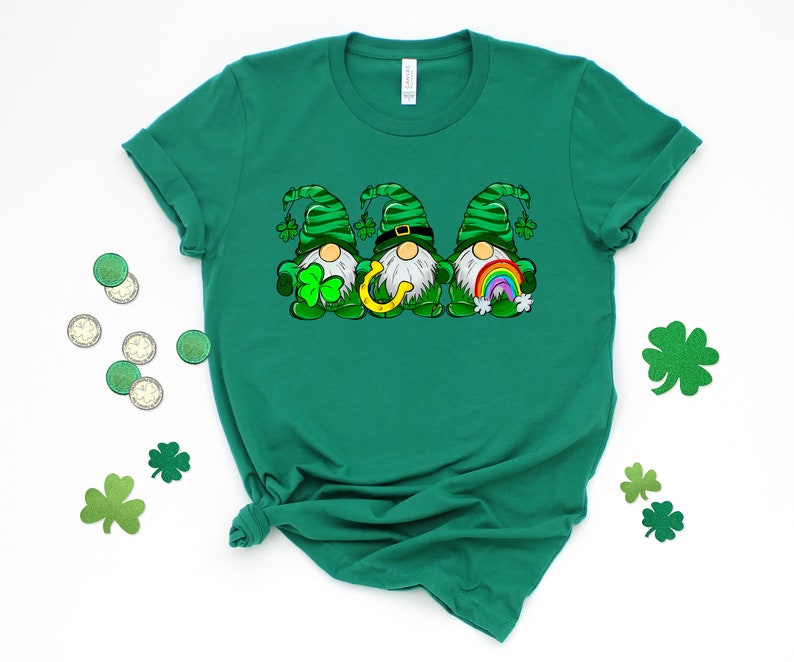 Peut inclure: T-shirt vert avec un motif de trois gnomes portant des chapeaux verts, tenant un fer &agrave; cheval, un arc-en-ciel et un tr&egrave;fle.