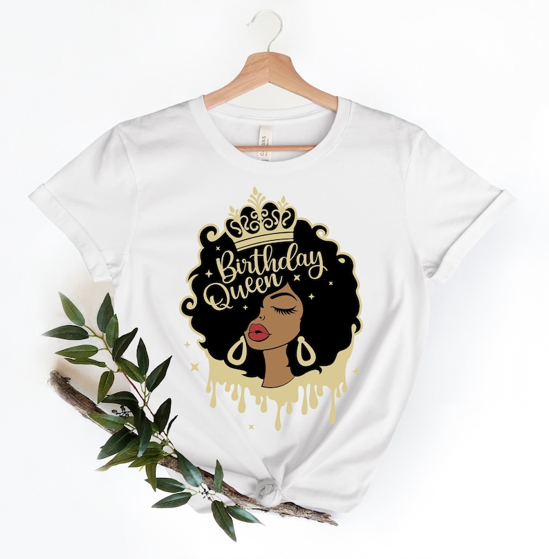 May include: White t-shirt with a gold graphic of a Black woman with a crown, closed eyes, and red lips. The text "Birthday Queen" is written in gold letters.
