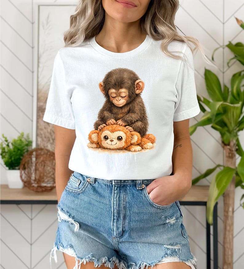 May include: White t-shirt featuring a watercolor illustration of two monkeys. One brown monkey is sitting on top of a smaller, orange monkey. The design has a cute, whimsical style, perfect for animal lovers.