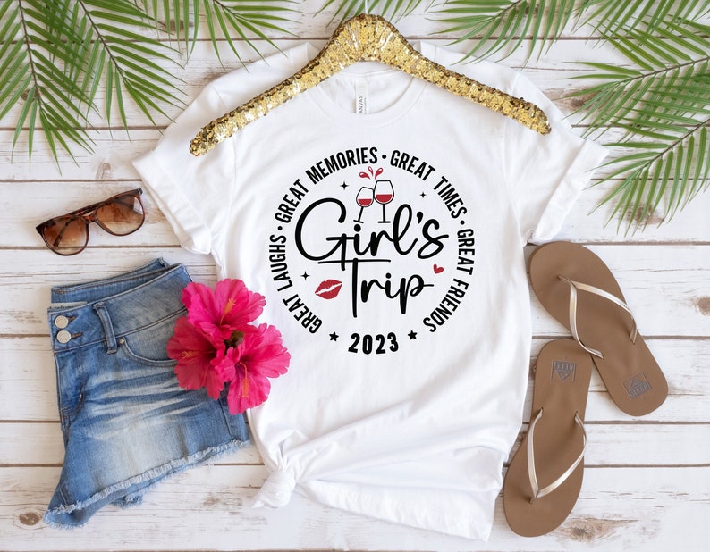 K&ouml;nnte beinhalten: Wei&szlig;es T-Shirt mit einem schwarzen Kreis-Motiv, auf dem "Great Laughs - Great Memories - Great Times - Great Friends" mit Weingl&auml;sern und einem roten Herzen steht. Der Text "Girl's Trip 2023" befindet sich in der Mitte des Kreises.