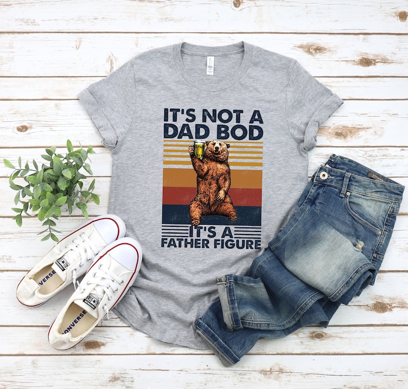 May include: A gray t-shirt with a vintage-style graphic of a bear holding a beer. The text on the shirt reads "It's not a dad bod, it's a father figure."