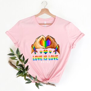 May include: Pink t-shirt with a rainbow heart design and the text "Love is Love Pride".