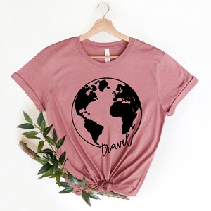 Peut inclure: Un t-shirt mauve avec un motif noir du monde et le mot "voyage" &eacute;crit en &eacute;criture cursive.