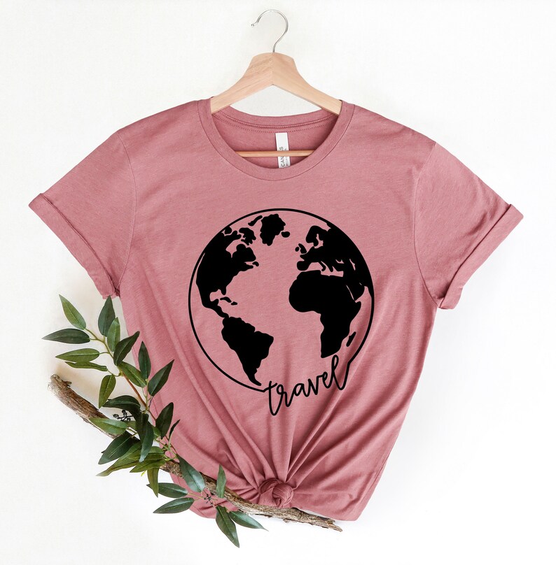 Peut inclure: Un t-shirt mauve avec un motif noir du monde et le mot "voyage" &eacute;crit en &eacute;criture cursive.