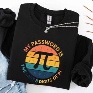 May include: Black sweatshirt with a colorful graphic that reads "MY PASSWORD IS THE LAST 8 DIGITS OF PI." The design features a Pi symbol and mathematical symbols within a circular design with orange, yellow, blue, and green stripes. A silver necklace rests on the sweatshirt.