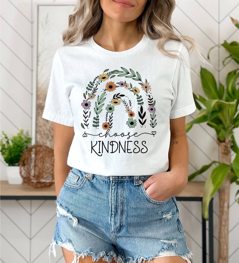 K&ouml;nnte beinhalten: Wei&szlig;es T-Shirt mit einem floralen Regenbogen-Design und dem Text "choose kindness" in Schwarz.