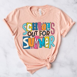 May include: A peach-colored t-shirt with the text "School's Out For Summer" in colorful, playful letters.