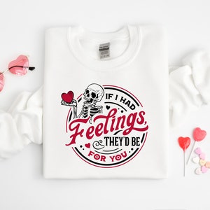 May include: White sweatshirt with a skeleton holding a red heart and the text "If I had feelings, they'd be for you".