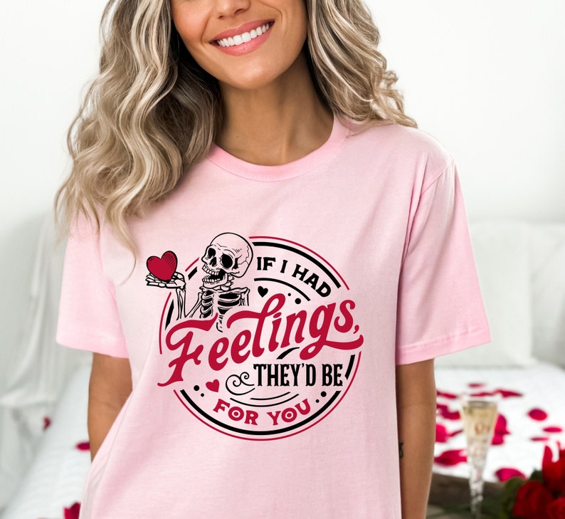 May include: Pink t-shirt featuring a black and white skeleton holding a red heart. The shirt has the text "If I had feelings they'd be for you" in a black circle with a red heart.