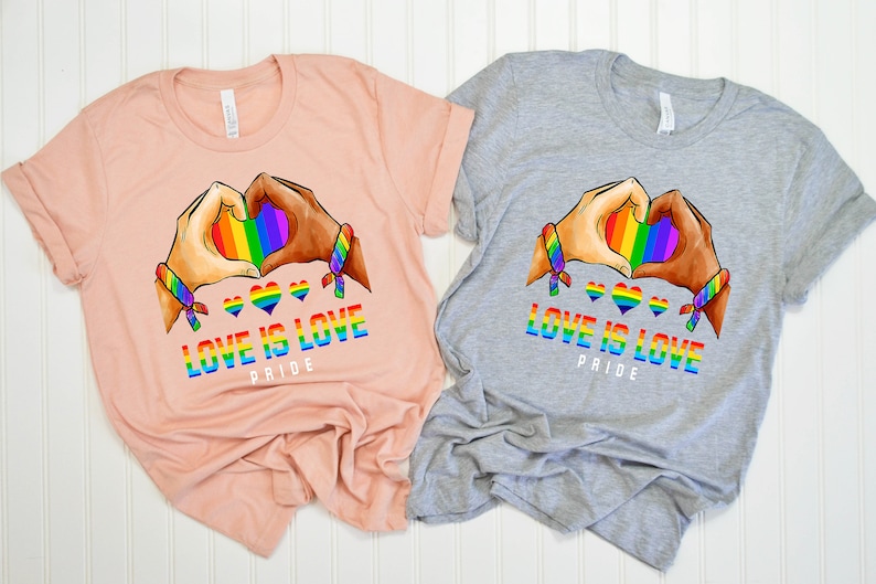 May include: Two t-shirts with a rainbow heart design and the text "Love is Love Pride". One shirt is peach and the other is gray.