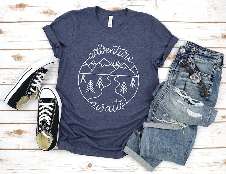 May include: A navy blue t-shirt with a white graphic of a mountain landscape and the text "adventure awaits".