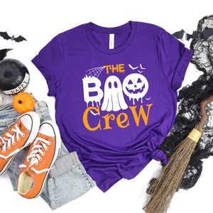 May include: Purple short-sleeved t-shirt with the text "The Boo Crew" in orange and white. A ghost with a dripping face and a jack-o-lantern are part of the design.