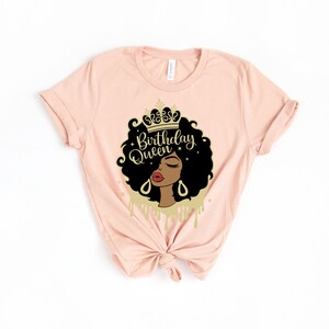May include: A pink t-shirt with a graphic of a Black woman wearing a gold crown. The graphic says "Birthday Queen" in gold lettering.