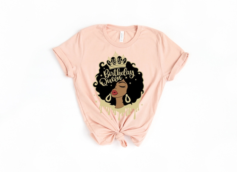 May include: A pink t-shirt with a graphic of a Black woman wearing a gold crown. The graphic says "Birthday Queen" in gold lettering.