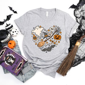 Może przedstawiać: Szary T-shirt z sercowatym wzorem przedstawiającym r&oacute;żne symbole Halloween, w tym ducha, kapelusz czarownicy, miotłę, czaszkę, pajęczynę, dynię, kukurydzę cukrową i słowo "Boo!"