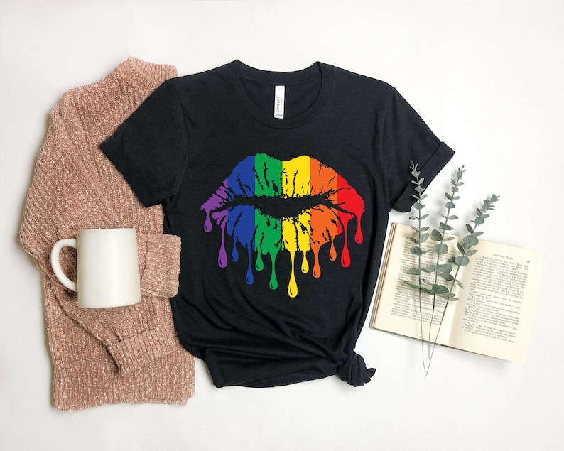 Op de afbeelding: Een zwart T-shirt met een regenboog druppelende kus grafische. De grafische is een gestileerde regenboog lip print met druppende verf.