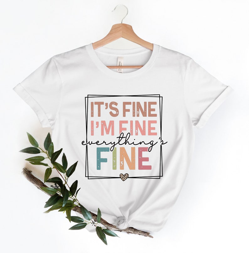 May include: White t-shirt with a graphic print that says "It's fine I'm fine everything's fine" in a colorful retro font with a small heart.