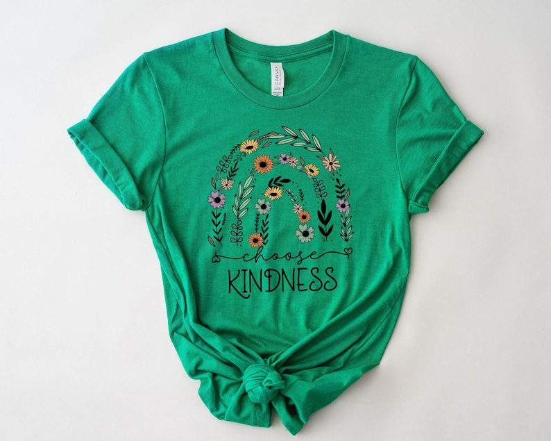 K&ouml;nnte beinhalten: Gr&uuml;nes T-Shirt mit einem floralen Regenbogen-Design und dem Text "choose kindness" in Schwarz.