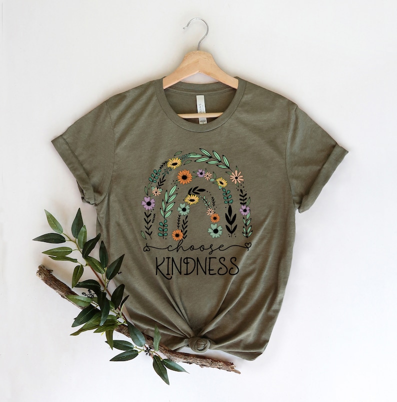 K&ouml;nnte beinhalten: Ein gr&uuml;nes T-Shirt mit einem floralen Regenbogen-Design und dem Text "choose kindness" in Schwarz.