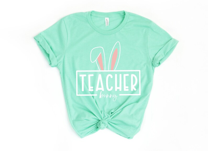 May include: A light green t-shirt with a white bunny ear design and the text "TEACHER bunny" in a white rectangle.