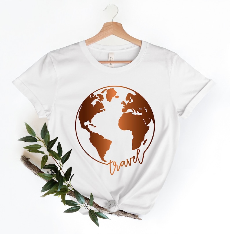 Peut inclure: T-shirt blanc avec un motif de globe terrestre de couleur cuivre et le mot "travel" &eacute;crit en dessous.