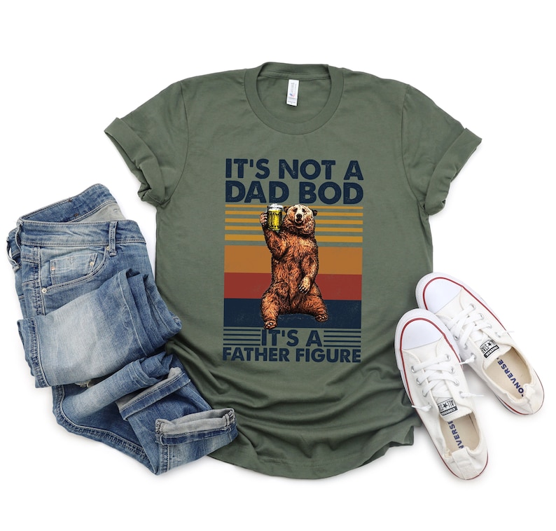 May include: A green t-shirt with a retro-style graphic of a bear holding a beer. The text on the shirt reads "It's not a dad bod, it's a father figure."