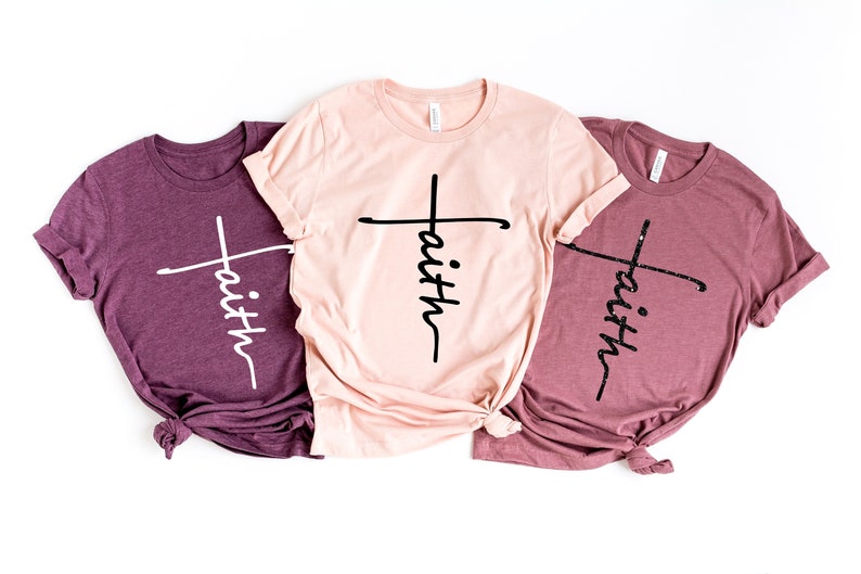 May include: Three t-shirts with the word "faith" written vertically with a cross in the middle. The shirts are in three different colors: maroon, pink, and light maroon.