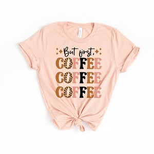 May include: A pink t-shirt with the text "But first, coffee" printed on it. The word "coffee" is repeated four times in a stacked design with a leopard print pattern.