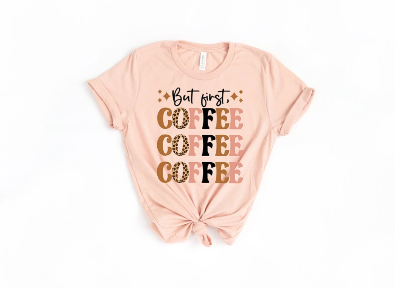 May include: A pink t-shirt with the text "But first, coffee" printed on it. The word "coffee" is repeated four times in a stacked design with a leopard print pattern.