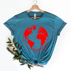 Peut inclure: T-shirt bleu sarcelle avec un globe terrestre rouge et le mot "travel" &eacute;crit en cursive rouge en dessous.