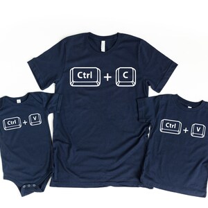 May include: Three navy blue t-shirts with white text and images of computer keys. The largest shirt says "Ctrl + C", the medium shirt says "Ctrl + V", and the smallest shirt says "Ctrl + V".