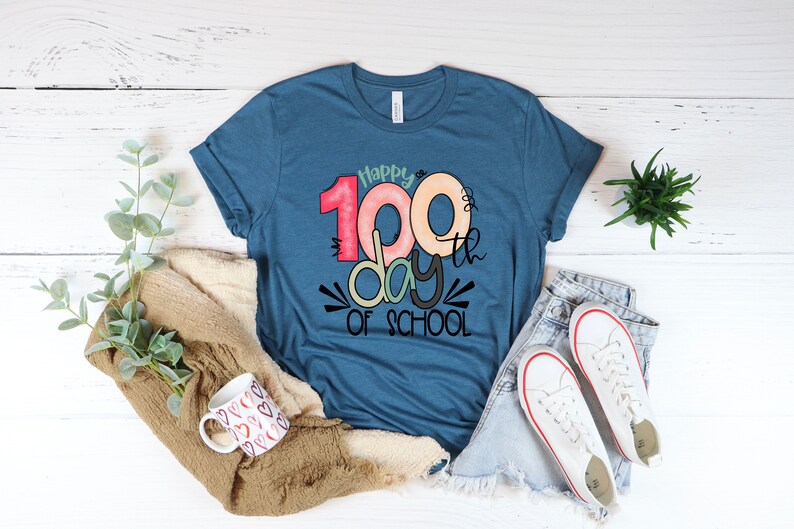 May include: A blue t-shirt with the text "Happy 100th day of school" in colorful, stylized lettering.
