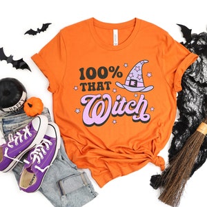 K&ouml;nnte beinhalten: Orangefarbenes T-Shirt mit einem pinkfarbenen und wei&szlig;en Hexenhut-Motiv und dem Text "100% That Witch".