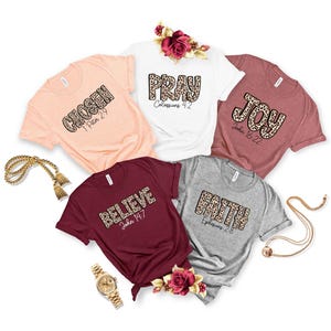 May include: Five short-sleeved t-shirts in peach, white, mauve, maroon, and grey. Each shirt features a leopard print word: CHOSEN 1 Peter 2:9, PRAY Colossians 4:2, JOY John 16:22, BELIEVE John 14:7, and FAITH Ephesians 2:8. Includes gold jewellery and roses.