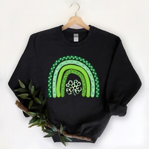 May include: Black sweatshirt with a green shamrock rainbow design. The rainbow is made up of three green arches with shamrock patterns.