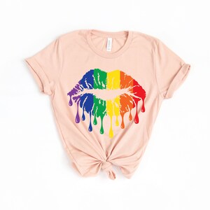 Op de afbeelding: Een lichtroze T-shirt met een regenboog druppelende kus grafische.