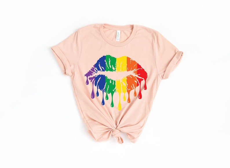 Op de afbeelding: Een lichtroze T-shirt met een regenboog druppelende kus grafische.