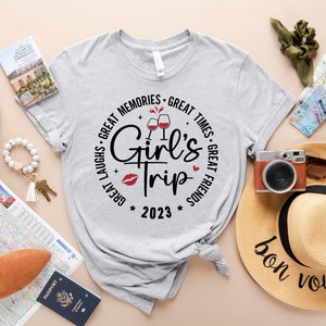 K&ouml;nnte beinhalten: Ein graues T-Shirt mit einem Kreisdesign, auf dem "Great Laughs - Great Memories - Great Times - Great Friends" mit einer Weinglasgrafik und dem Text "Girl's Trip 2023" steht.