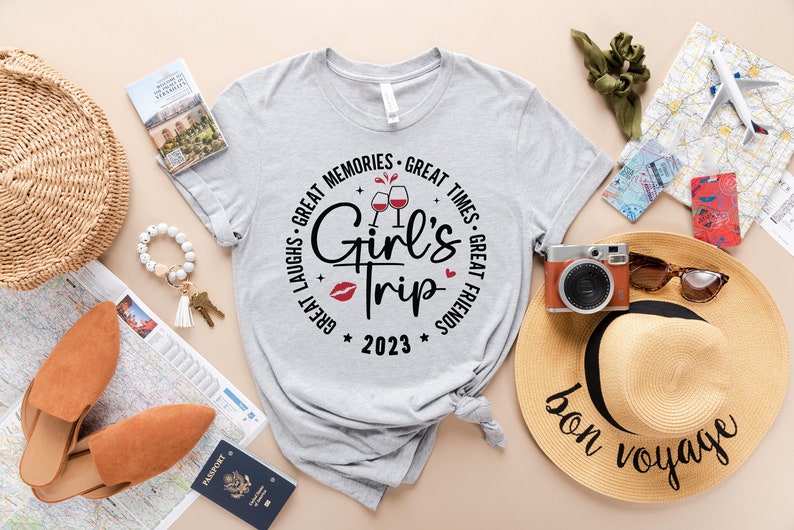 K&ouml;nnte beinhalten: Ein graues T-Shirt mit einem Kreisdesign, auf dem "Great Laughs - Great Memories - Great Times - Great Friends" mit einer Weinglasgrafik und dem Text "Girl's Trip 2023" steht.