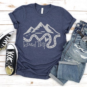 Puede incluir: Una camiseta azul marino con un gr&aacute;fico blanco de monta&ntilde;as y un camino sinuoso con el texto "Road Trip".