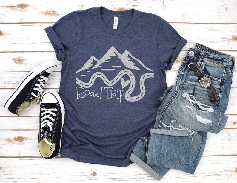 Puede incluir: Una camiseta azul marino con un gr&aacute;fico blanco de monta&ntilde;as y un camino sinuoso con el texto "Road Trip".