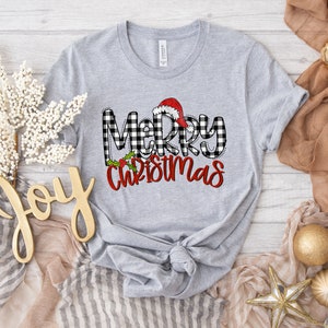 May include: Gray t-shirt with a black and white buffalo plaid design and the text "Merry Christmas" in red with a Santa hat on top of the "M".