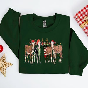 May include: A green Christmas sweater with a design of four cows wearing Santa hats and reindeer antlers. The cows are decorated with Christmas lights.